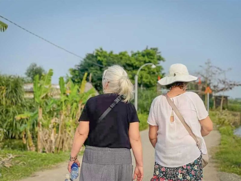 hue countryside tour 2 Two women walking through rural village paths surrounded by tropical greenery on a Hue countryside tour.