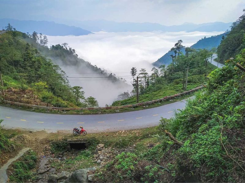 A road part of the Khau Pha Pass in Mu Cang Chai with motorbike parked and forest and mountain views on the background