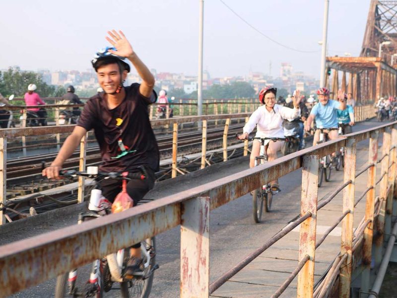 long bien bridge cycling tour hanoi 3 Local biking guide waving while leading tourists over Long Bien Bridge on a Hanoi bike tour