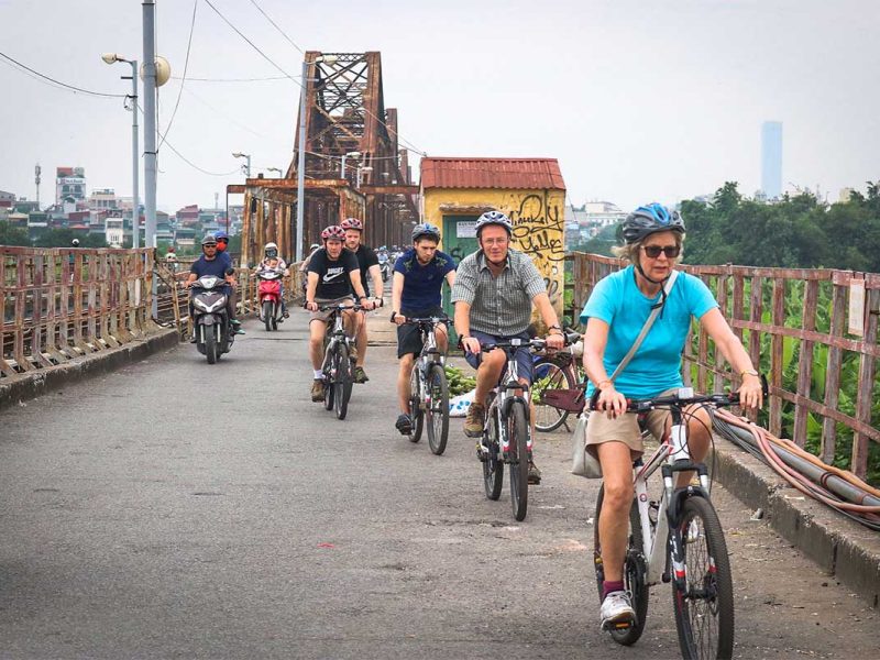 Cycling tour group riding across Long Bien Bridge during a Hanoi bike tour
