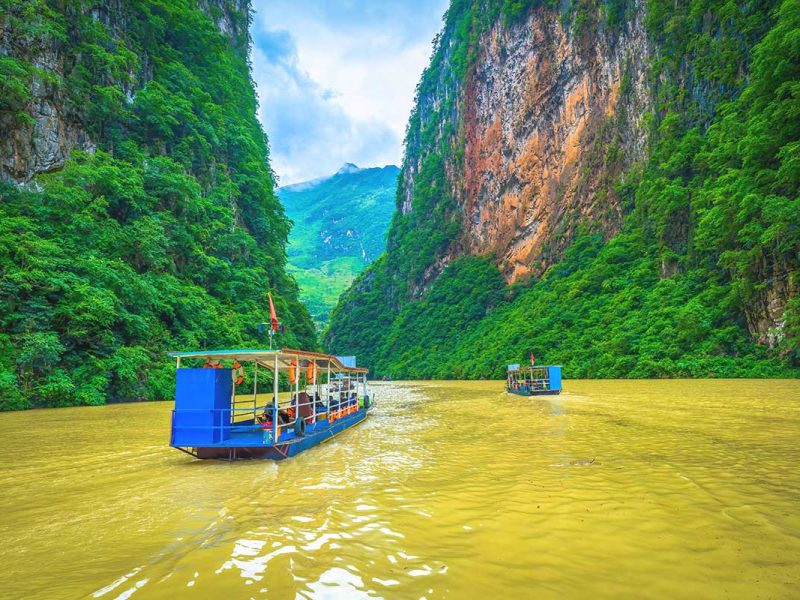 ma pi leng pass 9 A tourist boat cruising along the brown waters of the Nho Que River, passing between the towering cliffs of Ma Pi Leng Pass in Ha Giang.