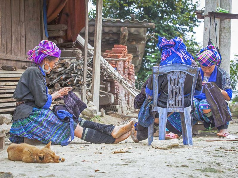 Local ethnic woman in traditional clothes are sitting in front of a house in a village in Mu Cang Chai district