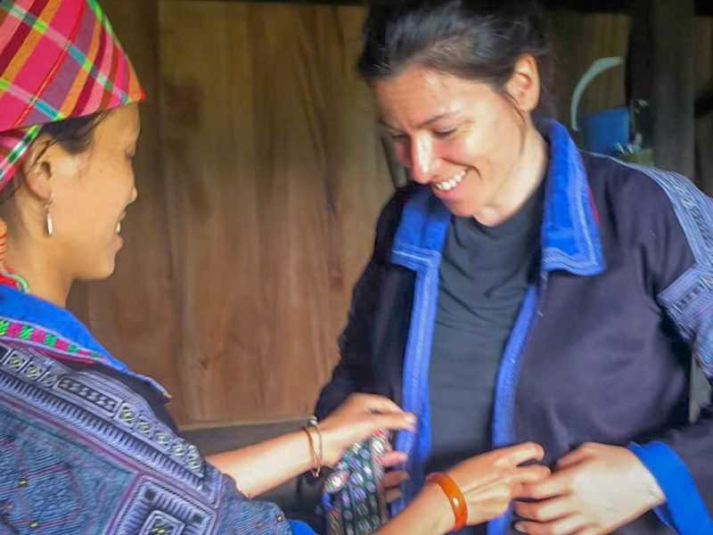 mu cang chai tour 15 Mu Cang Chai cultural tour homestay activity with a Hmong woman helping a traveler wear traditional clothing