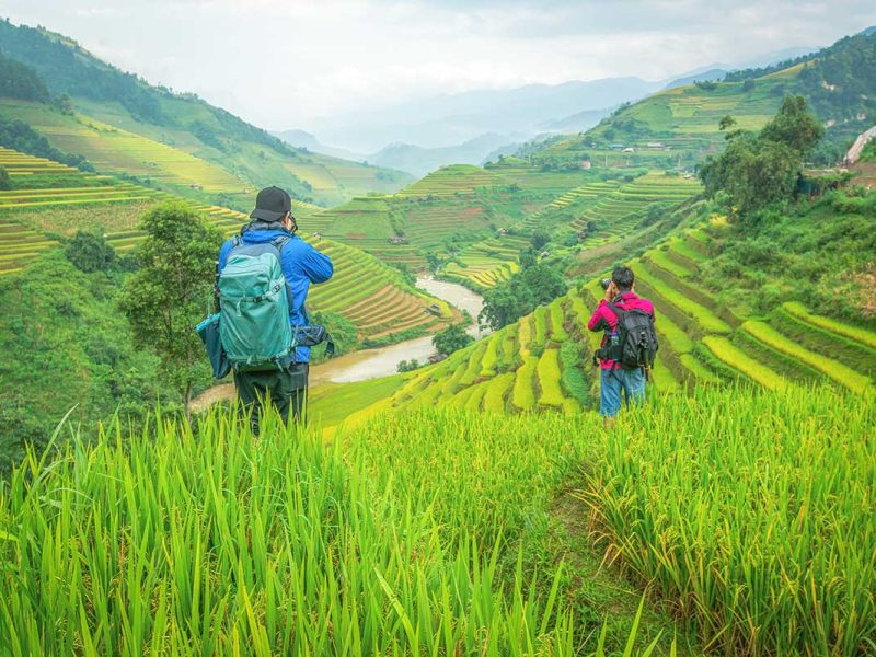 Two travellers wearing a small backpack making a trekking through the rice fields of Mu Cang Chai