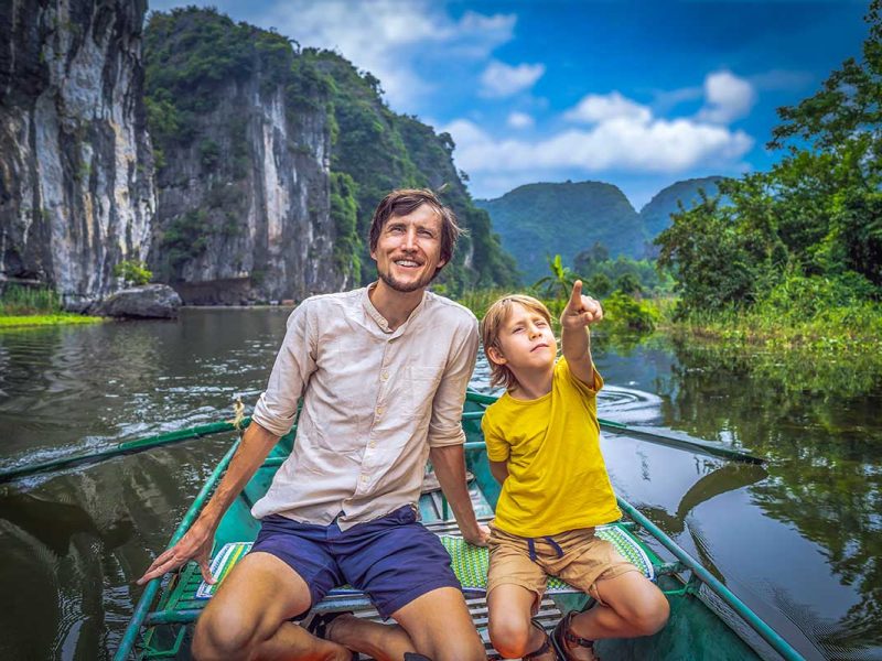 ninh binh with kids 1 A farther and son sitting in a scenic boat ride in Trang An, one of the best things to do in Ninh Binh with kids