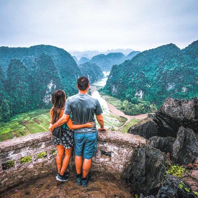 A romantic view of a couple on their honeymoon in Vietnam overlooking the rice fields from Mua Cave at sunset in Ninh Binh