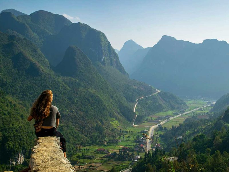 vietnam solo female traveler ha giang valley Solo female traveler sitting on a rock, admiring the stunning valley views in Ha Giang, Vietnam.